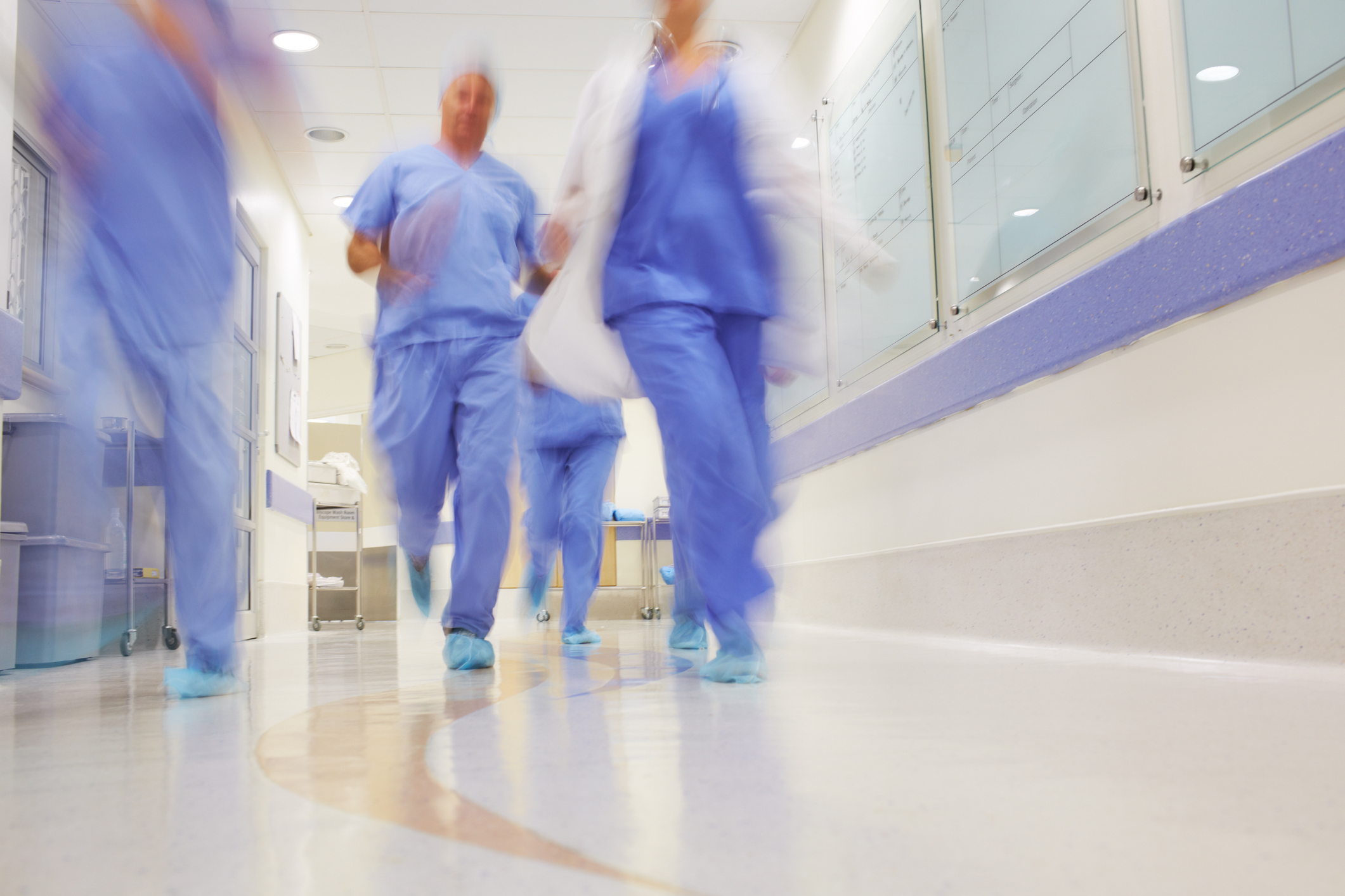 Travel nurses wearing blue scrubs in hospital rushing pass each other. 